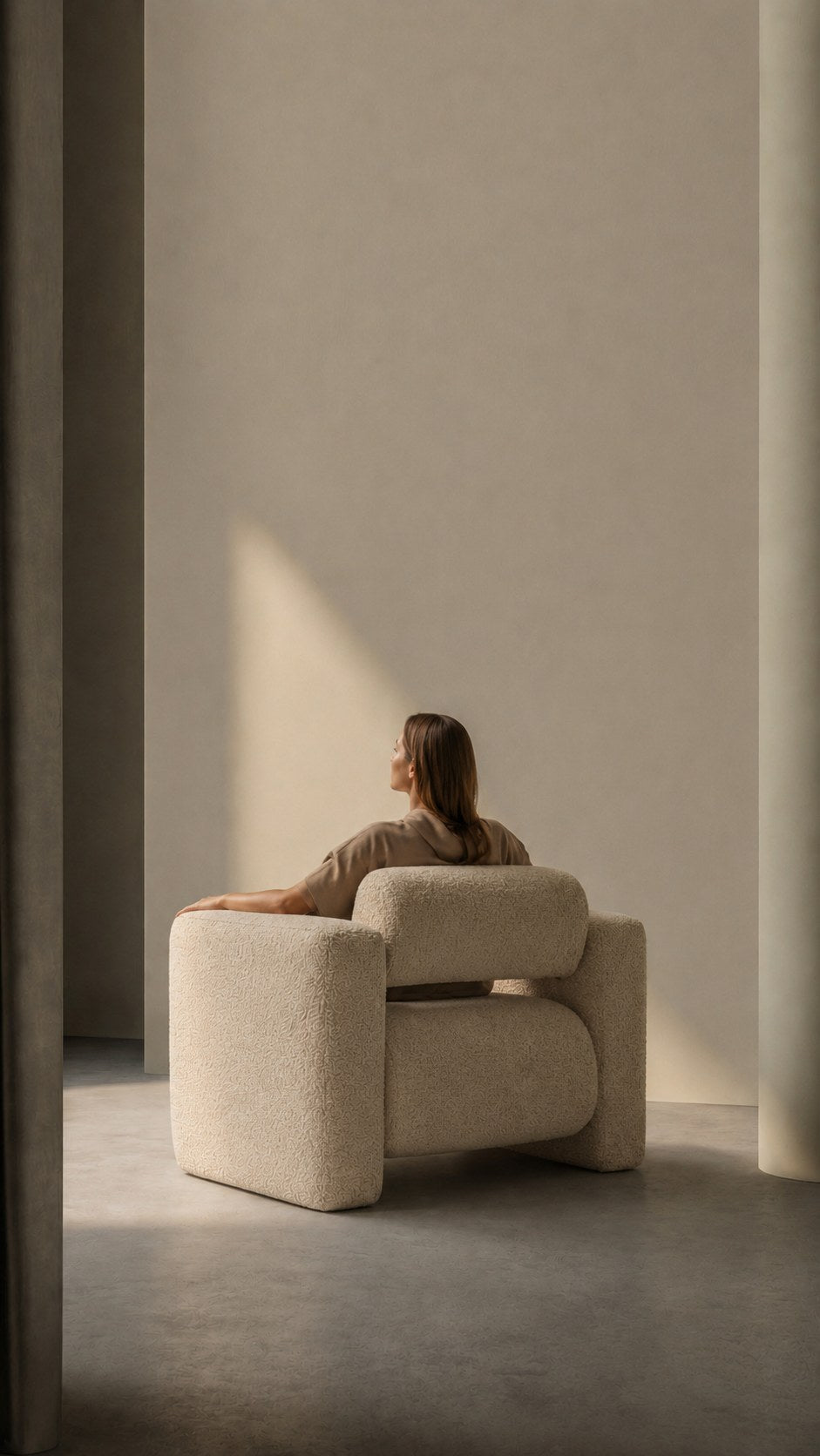 Persona sentada en un sillon tapizado dentro de un espacio iluminado con luz natural